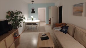 A living room with a sofa, a coffee table, a TV, a dining table with chairs, a hanging light fixture, and a plant.