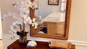 A wooden console table with a mirror, a vase with white flowers, and a woven basket.