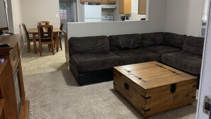 Ein Wohnzimmer mit einem Ecksofa, einer Holzkiste und einem Essbereich mit Stühlen und einem Tisch.
