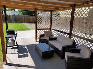 Un patio al aire libre con mobiliario de mimbre y una parrilla.