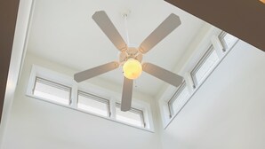 Una stanza con ventilatore a soffitto, un lucernario, una TV a schermo piatto montata a parete e una porta che dà su un'altra stanza.