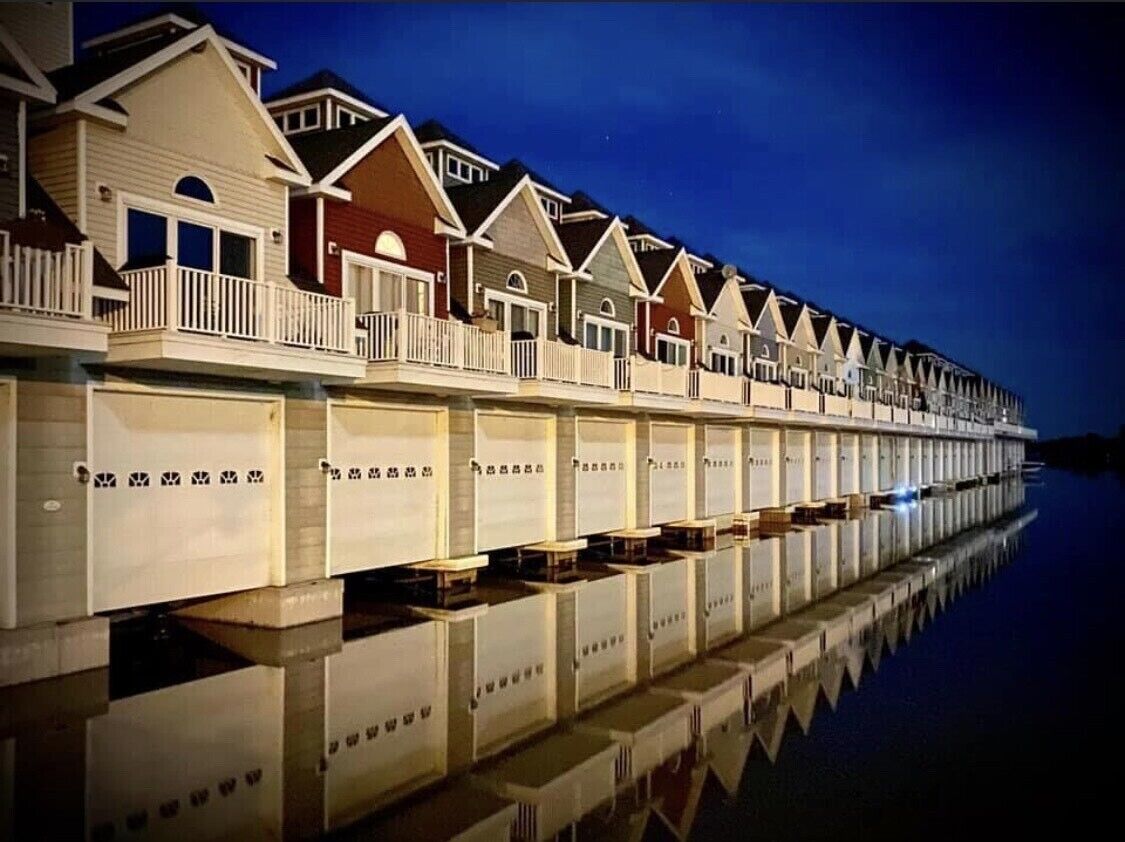 A row of waterfront condominiums with balconies, reflecting on the water.