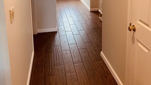 Un corridoio con pavimento in legno, pareti bianche e una porta bianca in fondo.