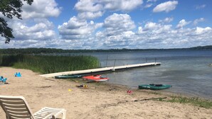 A sandy beach with a row of kayaks and a dock extending into the water.