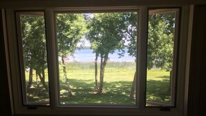 A room with a large window overlooking a grassy area with trees and a body of water.
