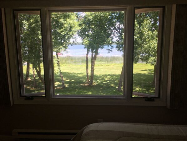 A room with a large window overlooking a grassy area with trees and a body of water.