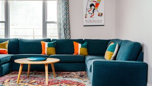 A modern living room with a teal sectional sofa, a round wooden coffee table, and a colorful patterned rug. - The Blue Door Bentonville is an ideal Bike In/Bike Out location, close to dwtwn. (Bentonville)