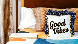 A neatly made bed with a pillow featuring the text "Good Vibes" and a decorative pom-pom. - The Blue Door Bentonville is an ideal Bike In/Bike Out location, close to dwtwn. (Bentonville)