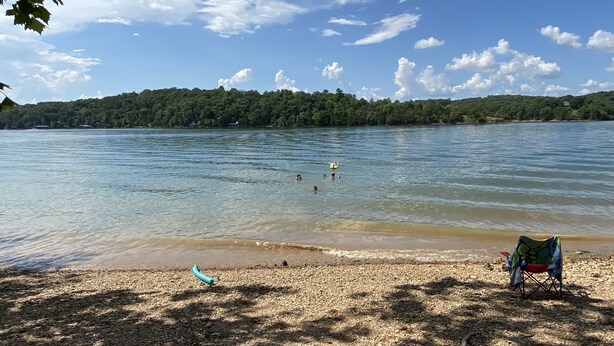 A beach with a clear view of the lake, a chair, and a small boat. - The Blue Door Bentonville is an ideal Bike In/Bike Out location, close to dwtwn. (Bentonville)