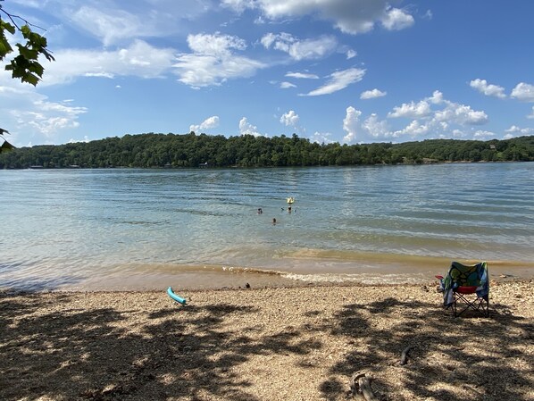 A beach with a clear view of the lake, a chair, and a small boat.