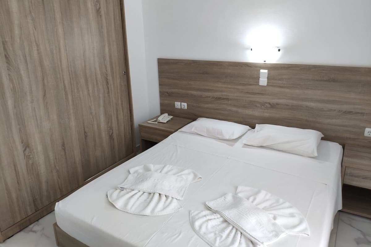 A hotel room with a wooden headboard, a bedside table with a phone, and a neatly made bed with white linens and towels.