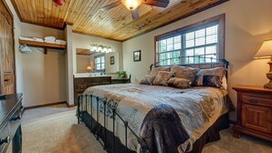 Une chambre avec un grand lit, un plafond en bois et une fenêtre équipée de stores.