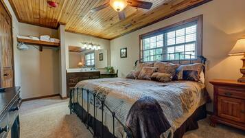 A bedroom with a large bed, wooden ceiling, and a window with blinds.