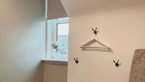 Une pièce avec un plafond en pente, une fenêtre donnant sur un beau paysage, une chaise et des crochets fixés au mur.