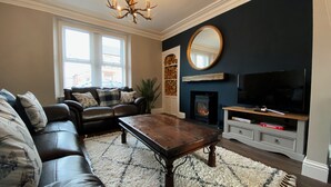 Un salon avec un canapé en cuir, une table basse en bois, une cheminée, un téléviseur et un grand miroir au mur.