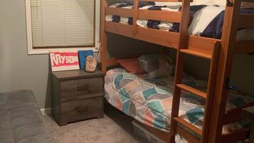 A bunk bed room with a desk and drawers, a window with blinds, and a ceiling fan.