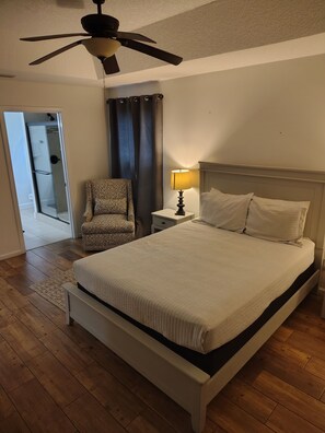 A bedroom with a bed, a chair, a nightstand, a lamp, a ceiling fan, and a door leading to a bathroom. - Modern, Upscale, and New "Blue Bungalow" in the heart of Downtown St Augustine (St. Augustine)