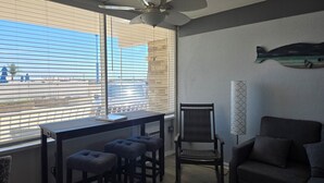 Una habitación con un escritorio, dos taburetes, una silla, un cuadro de peces y una ventana con persianas.