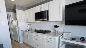 Una cocina moderna con armarios blancos, un refrigerador de acero inoxidable, un microondas y una estufa a gas.