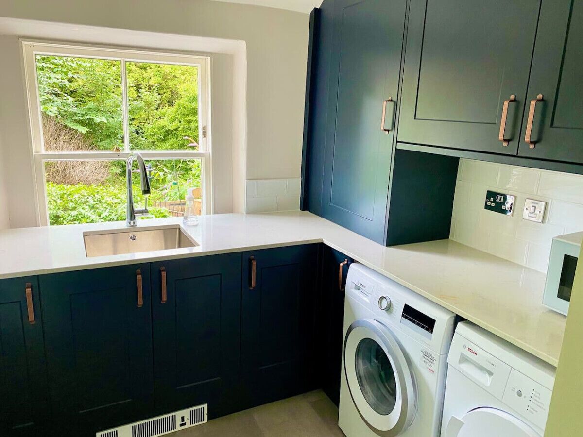 A compact kitchen with dark cabinets, a washing machine, and a window with a view of greenery.
