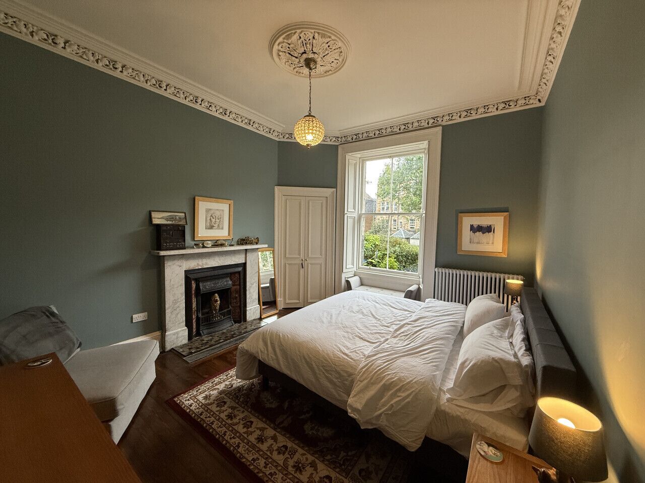 A bedroom with a large bed, a fireplace, a window with a view, and a ceiling light.