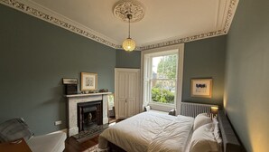 A bedroom with a large bed, a fireplace, a window with a view, and a ceiling light. - Meadows Sanctuary-Perfect base for exploring Edinburgh, private  garden (Edinburgh)