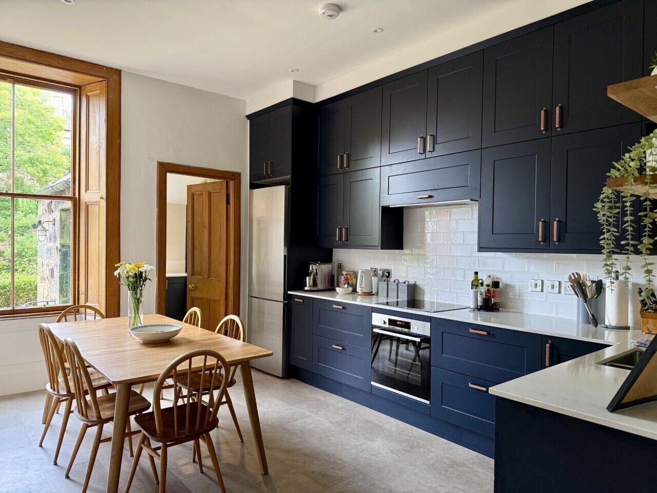 A modern kitchen with dark cabinetry, a central island, and a dining area with wooden chairs and a table.