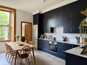 A modern kitchen with dark cabinetry, a central island, and a dining area with wooden chairs and a table.