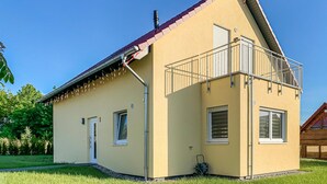 Ett tvåvåningshus med ett rött tak, en balkong med metallräcken och en liten trädgård.
