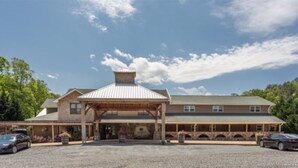 A two-story building with a covered entrance and a stone facade. - Charming  Cottage at Willow Creek Falls & Vineyard in Blue Ridge, GA (Blue Ridge)