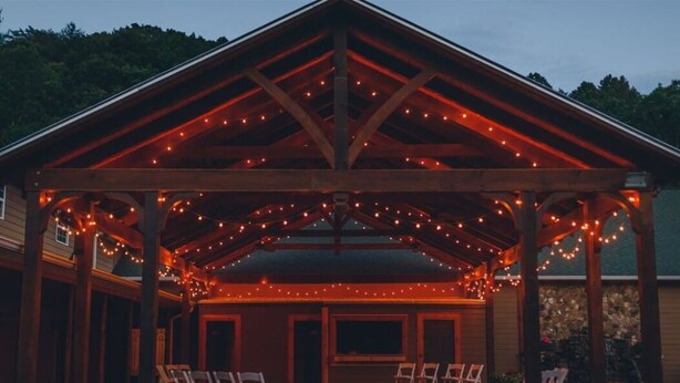 A wooden pavilion with a covered seating area, surrounded by stone steps and decorative lights. - Charming  Cottage at Willow Creek Falls & Vineyard in Blue Ridge, GA (Blue Ridge)