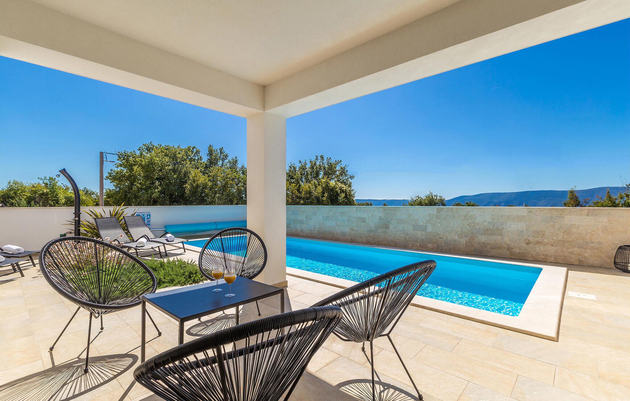 A covered outdoor area with a pool, lounge chairs, and a table with drinks.