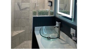 Un baño moderno con cabina de ducha de vidrio, tocador con lavabo de cristal e un espejo grande con iluminación LED.