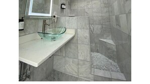 Un baño moderno con tragaluz, un lavamanos de vidrio y paredes de mármol.