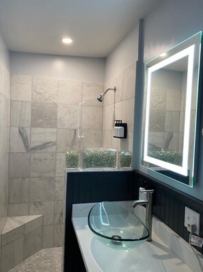 Un baño moderno con cabina de ducha de vidrio, tocador con lavabo de cristal e un espejo grande con iluminación LED.