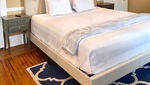 Un dormitorio con cama, mesitas de noche, una puerta e iluminación en la pared.