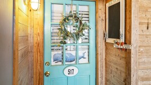 A turquoise door with a number plate '517', a decorative wreath, and a sign that reads 'DON'T BE CRABBY... YOU'RE AT THE BEACH.'