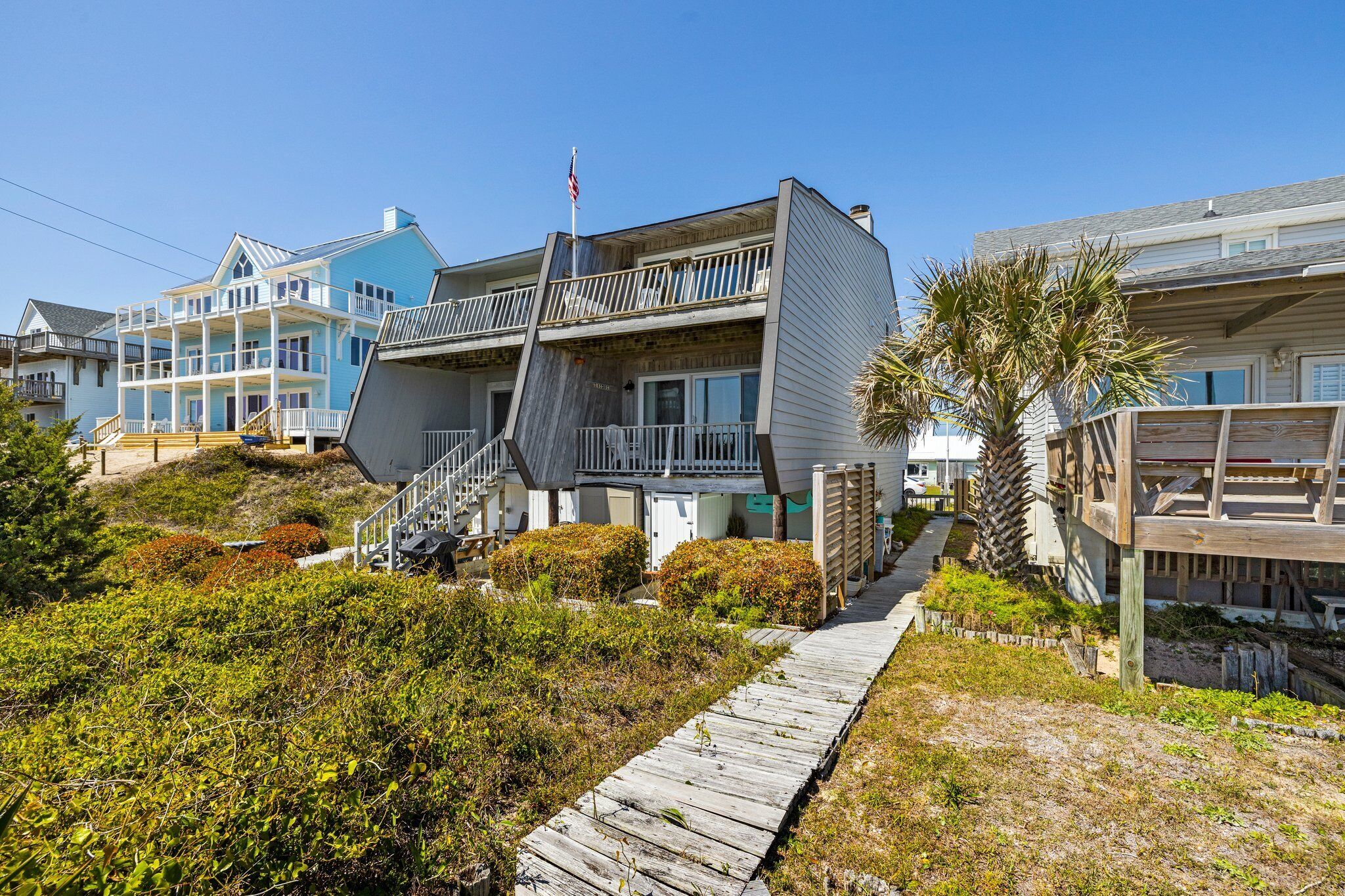 A beachfront property with a wooden deck, a staircase leading to a balcony, and a view of the ocean.