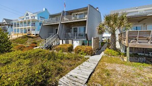 A beachfront property with a wooden deck, a staircase leading to a balcony, and a view of the ocean.