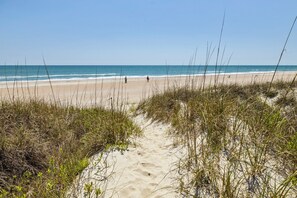 A sandy beach with sparse vegetation and a clear view of the ocean. - Whimsical Whale - Oceanfront Apartment (Atlantic Beach)