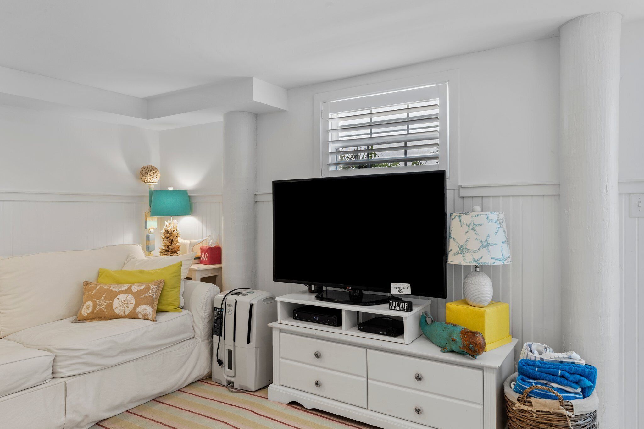 Een moderne woonkamer met een flatscreen televisie, witte meubels, een lamp en een mand vol opgevouwen kleding.