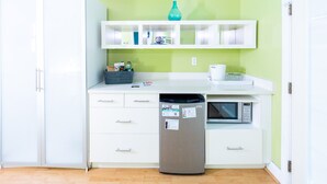 Een compacte keuken met witte kasten, een magnetron, een vaatwasser en een groene wand.