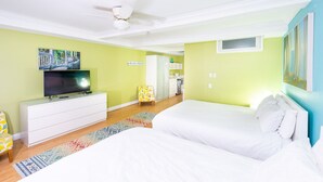 Een slaapkamer met een bed, een televisie, een plafondventilator en een keuken op de achtergrond.