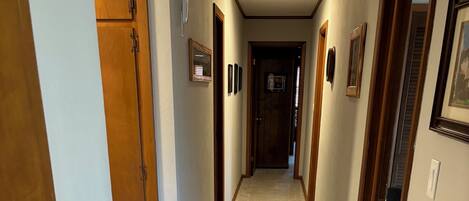 A narrow hallway with carpeted floors, wooden doors, and framed pictures on the walls.