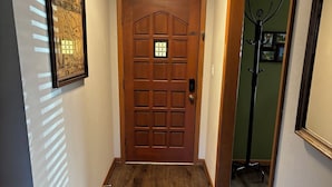 Een gang met een houten deur, een lijst met een afbeelding aan de muur en een kapstok in de hoek.