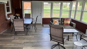 Een wintertuin met een eettafel, stoelen, een bank en een plafondventilator.