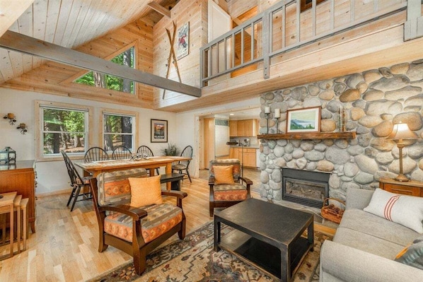 A spacious living area with a stone fireplace, wooden furniture, and a high ceiling with exposed beams.