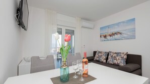 A modern living room with a white dining table, a vase with flowers, and a painting of a lighthouse on the wall. - Beautiful apartment in Podaca with WiFi (Podaca)
