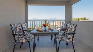 A balcony with a table set for two, chairs with floral upholstery, a fruit bowl, and a view of the sea and mountains. - Beautiful apartment in Podaca with WiFi (Podaca)