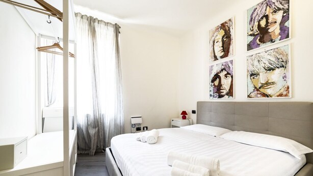 Une chambre d’hôtel avec un lit, une table de chevet, une lampe rouge et une fenêtre avec des rideaux.